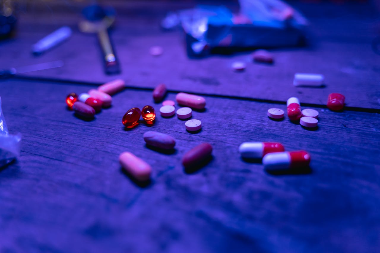 A variety of capsules and pills scattered on a wooden surface under blue lighting.