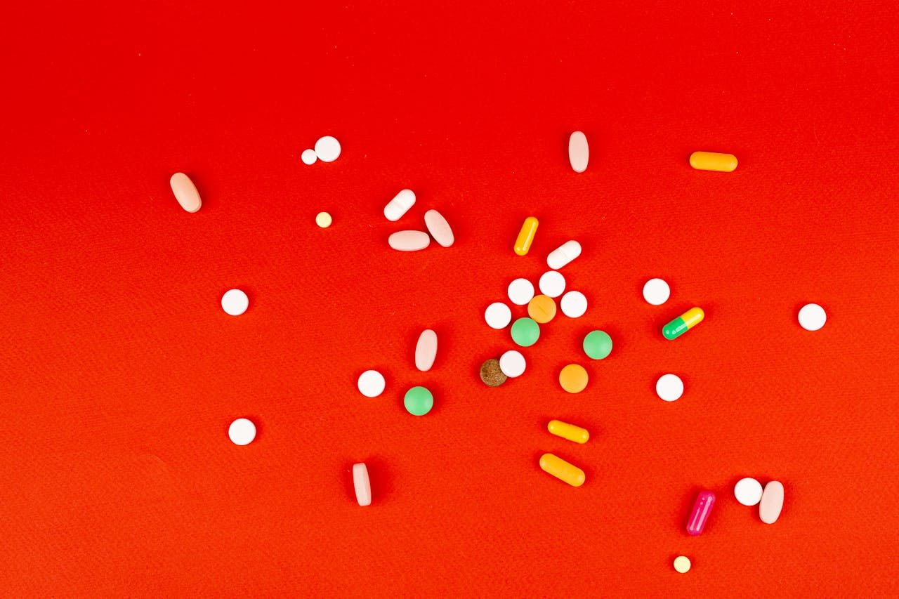 A variety of pills scattered on a vivid red surface, showcasing different shapes and colors.