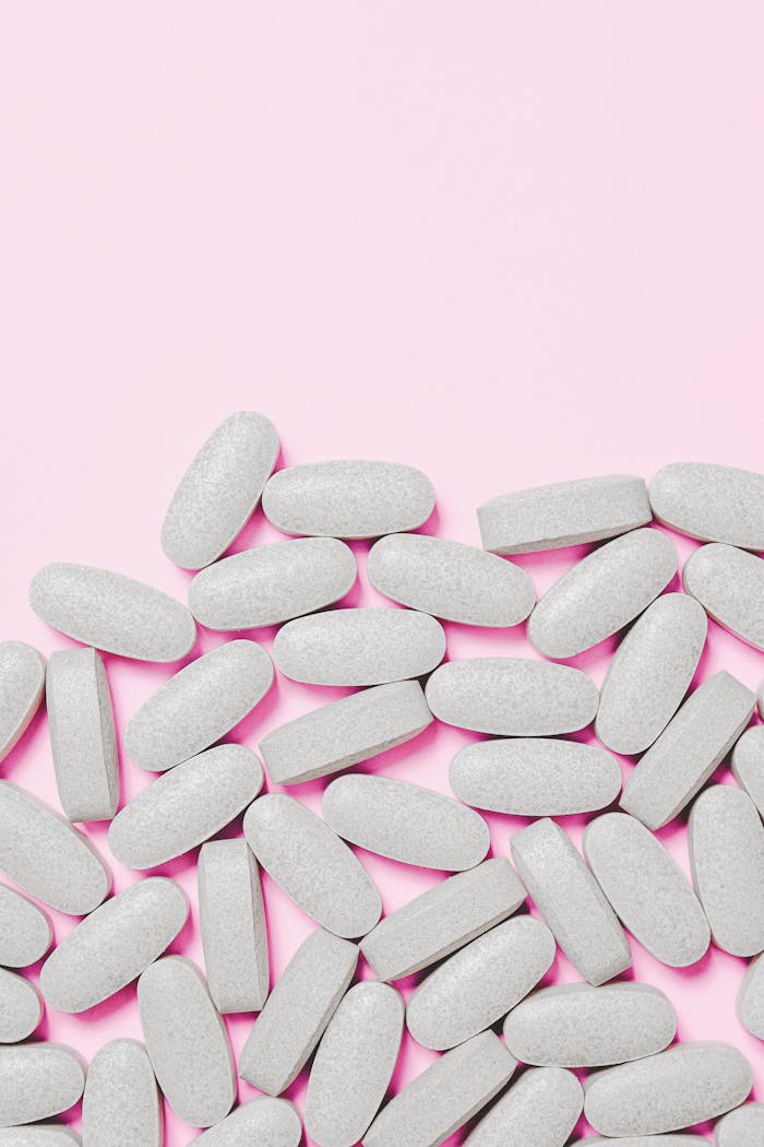 Scattered white pills on a soft pink background, representing healthcare and medication.